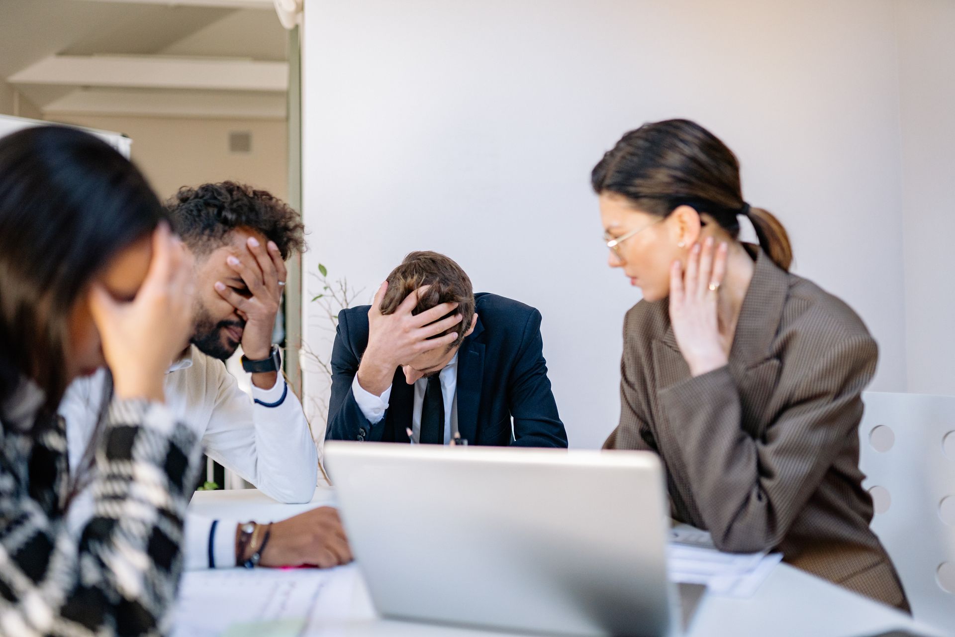 Four stressed business professionals around a meeting table with heads in their hands after a failed sales hire