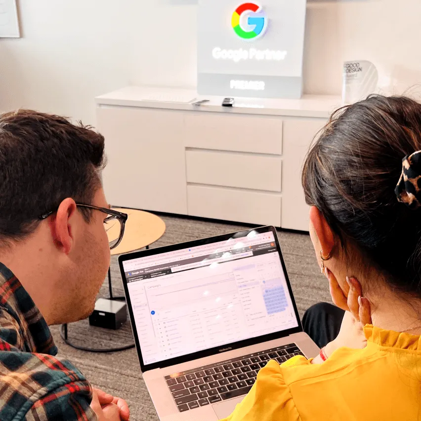 Two people look at a laptop screen displaying an analytics dashboard, with a Google Partner Premier sign visible in the background.