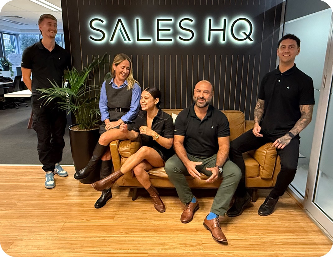 Sales HQ Team laughing with logo sign on office wall in background